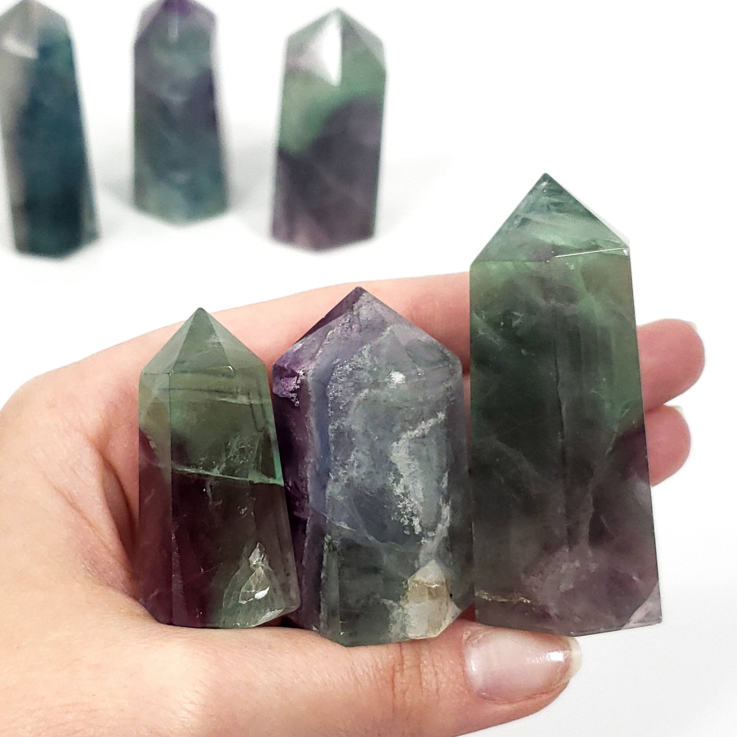 Hand holding a stack of multicolored crystal points against a white background