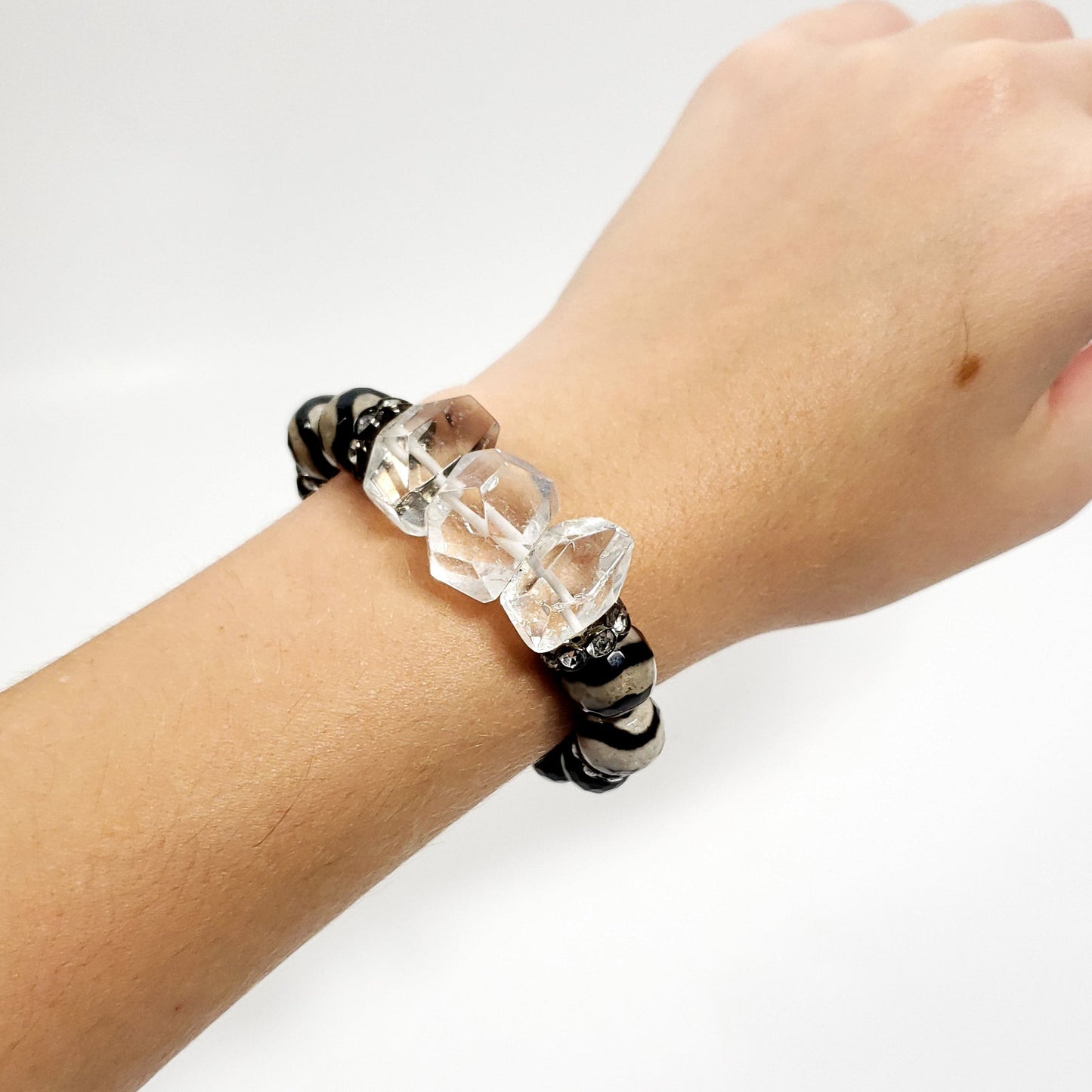 Hand wearing a bracelet with clear beads on a white background