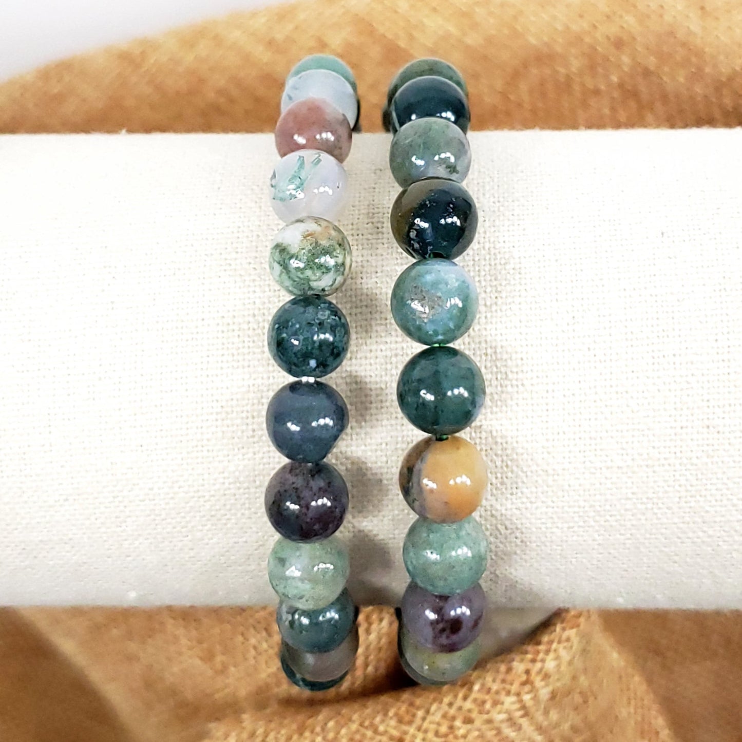 Set of three beaded bracelets on a white candle with a brown fabric background