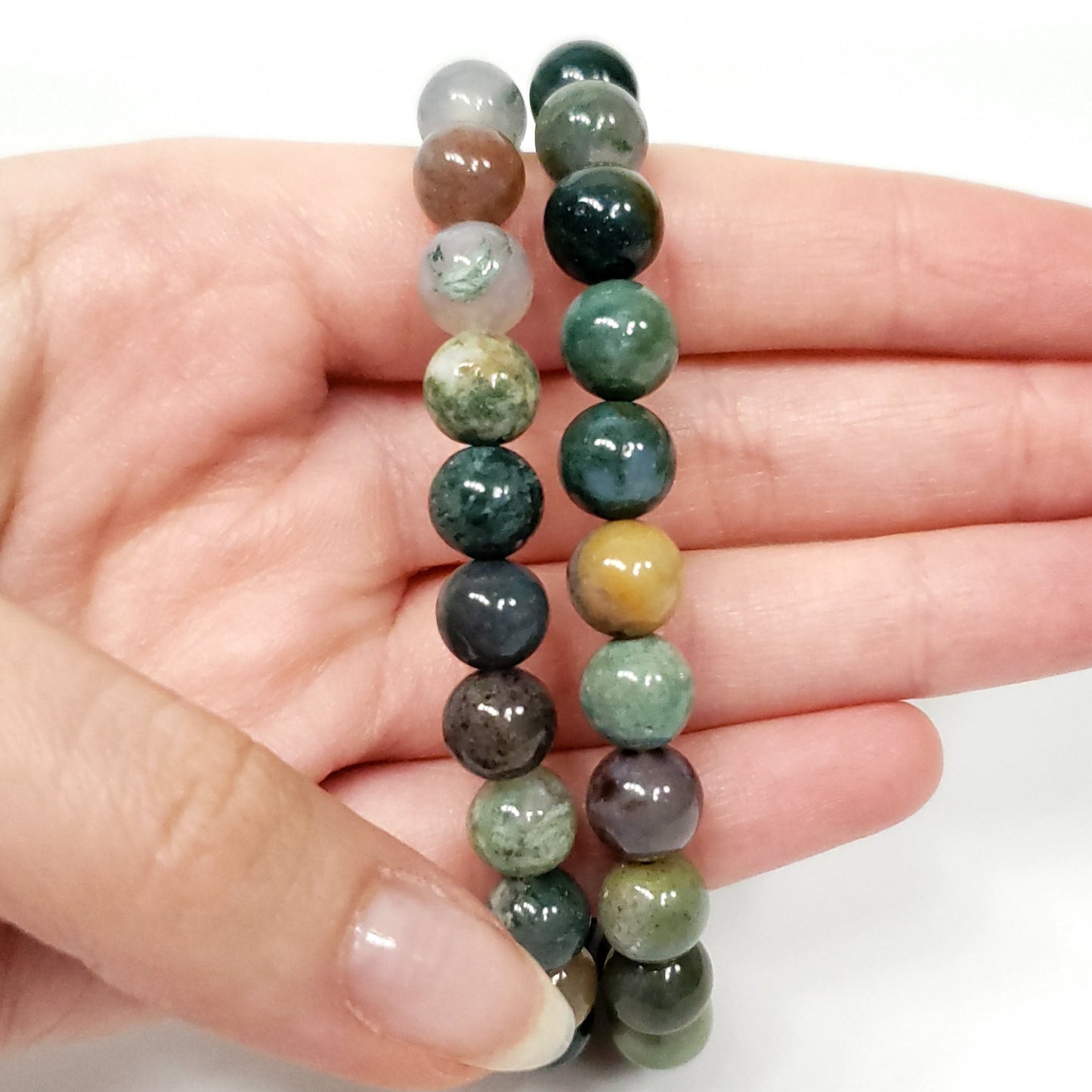 Hand holding a pair of green beaded bracelets on a white background
