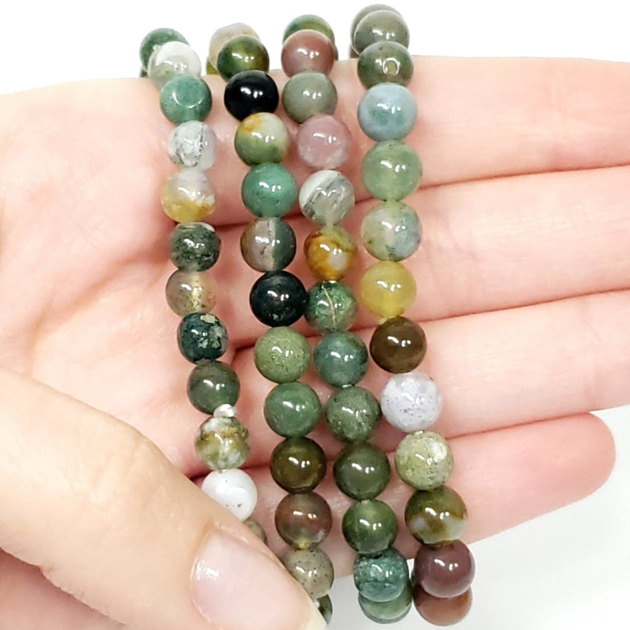 Hand holding a stack of green beaded bracelets on a white background