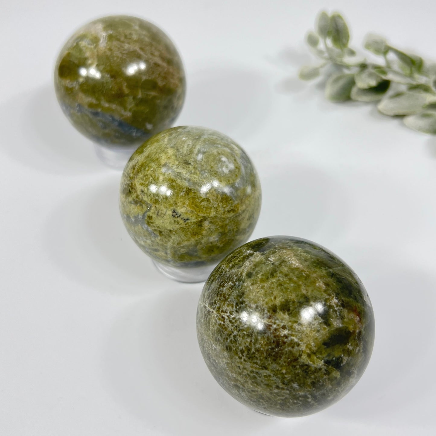 Three green marbled stones on a white surface with a small plant.