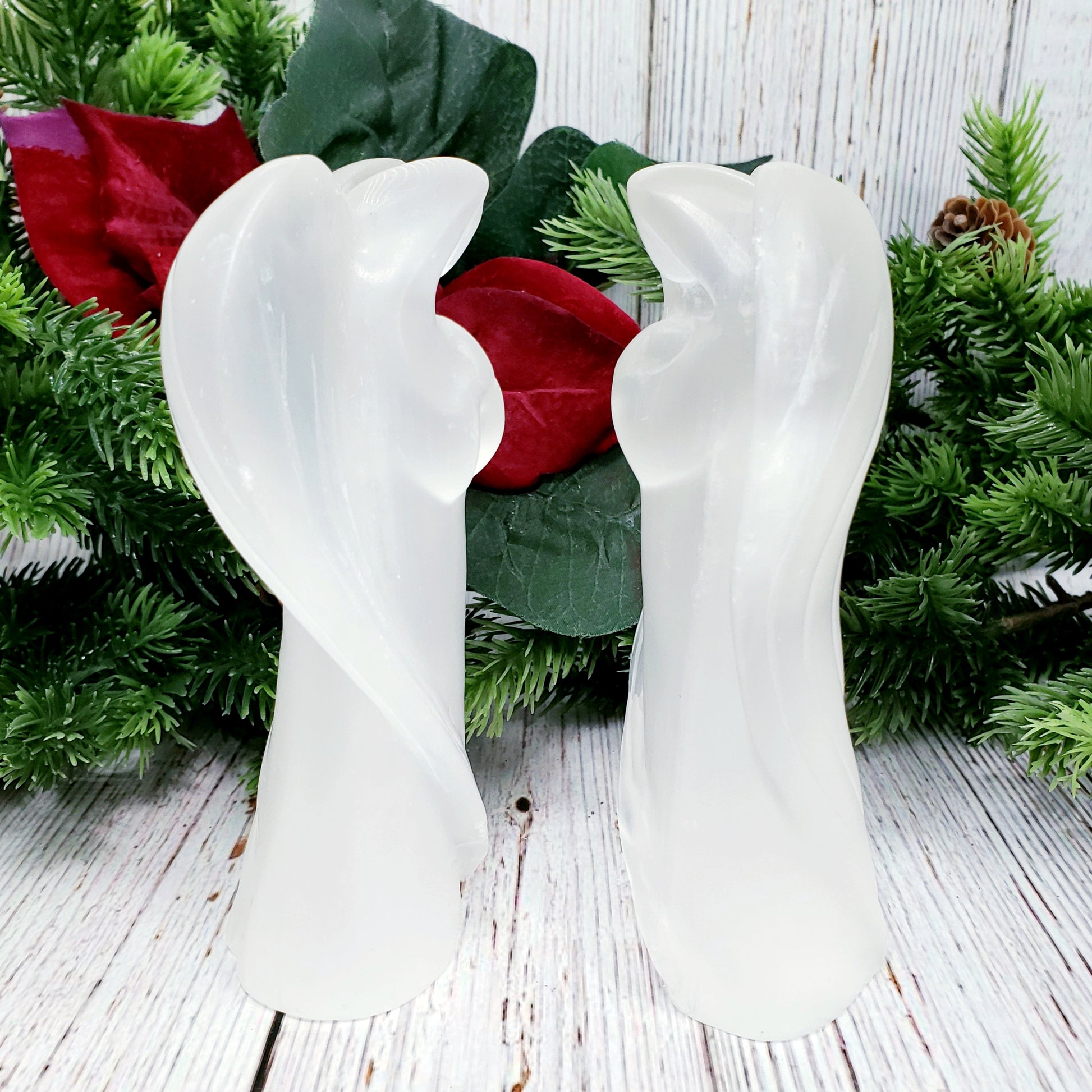 Two large selenite angels facing each otehr with christmas greenery in background