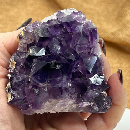 Amethyst crystal held in a hand against a gold fabric background