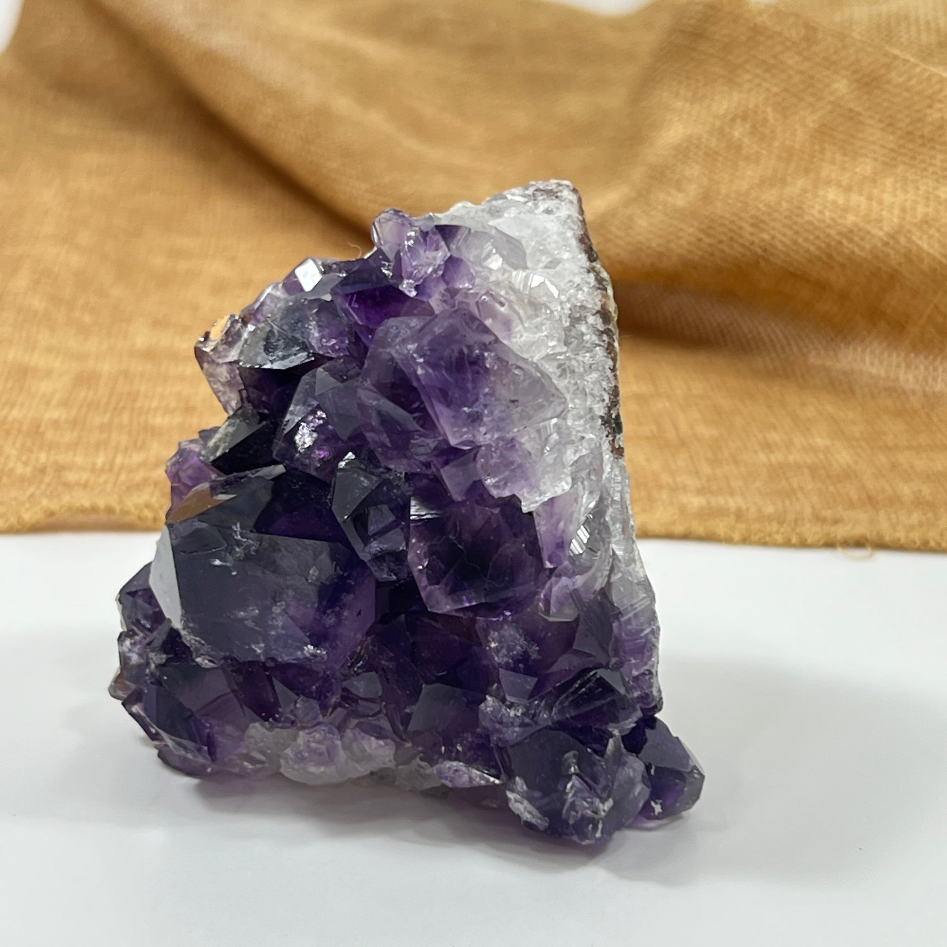 Amethyst crystal cluster on a white surface with a gold fabric background