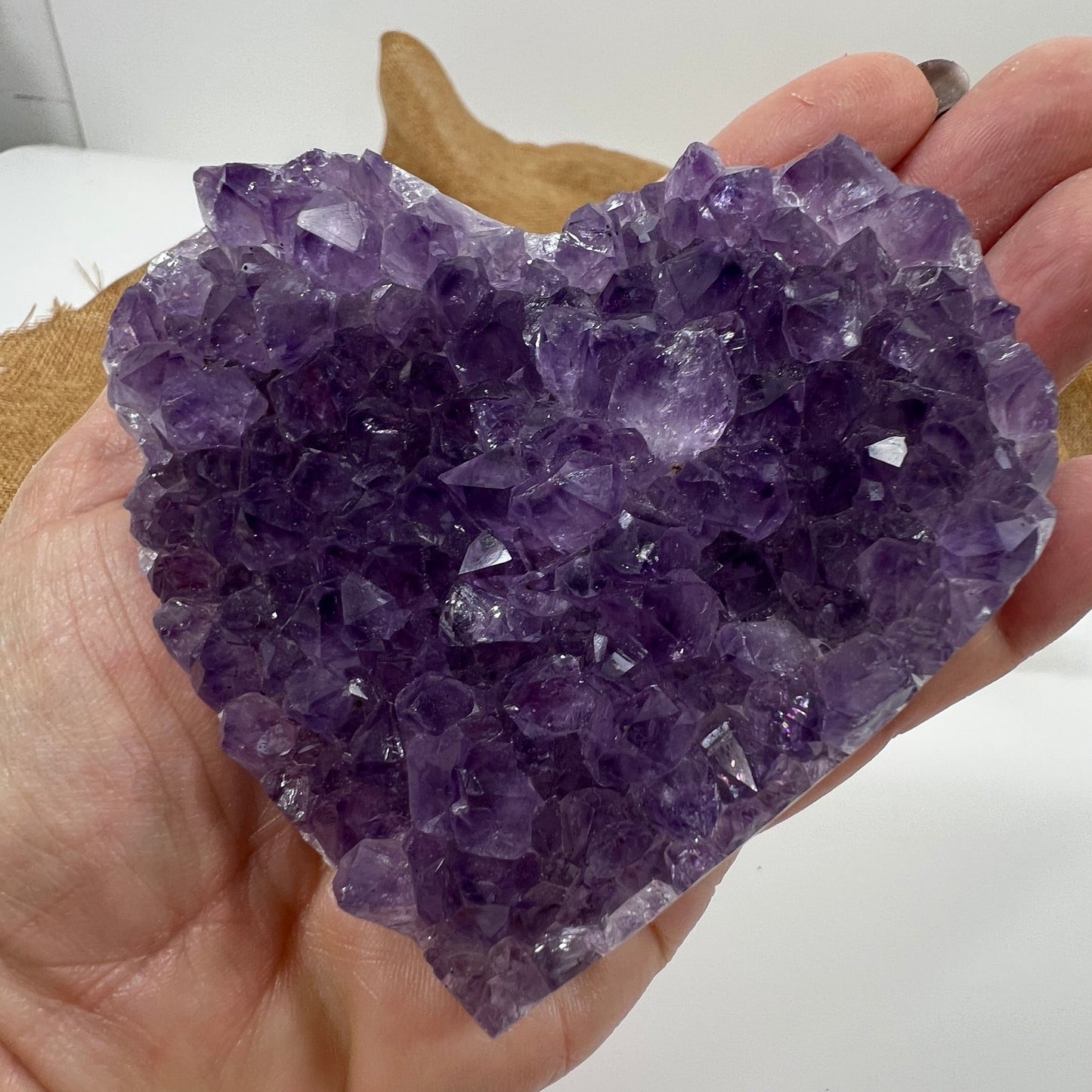 Hand holding a large purple crystal cluster against a neutral background