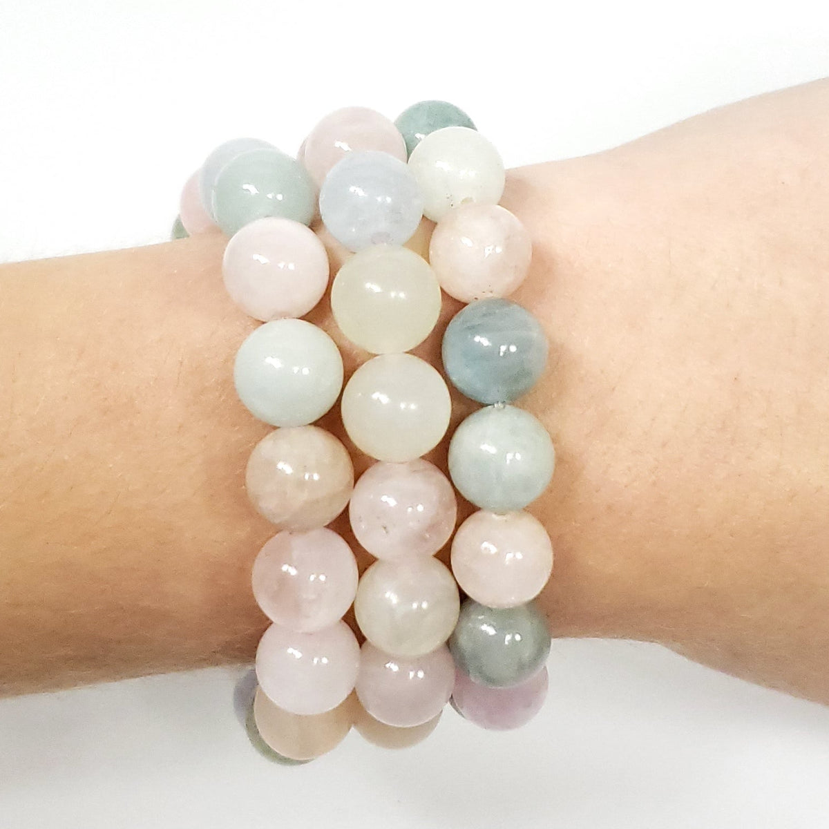 Three 10mm Morganite beaded stretch bracelets in pastel pink, pale green, and cream tones worn on a person's wrist against a plain white background.