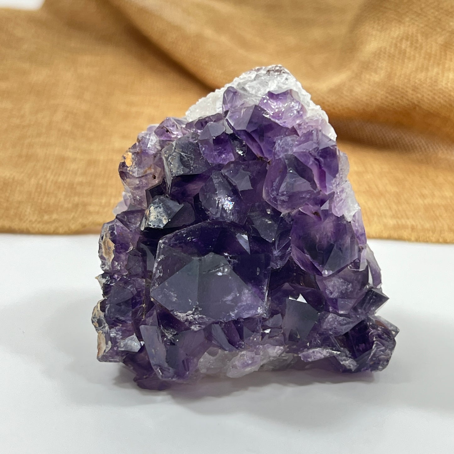 Amethyst crystal cluster on a white surface with a gold fabric background