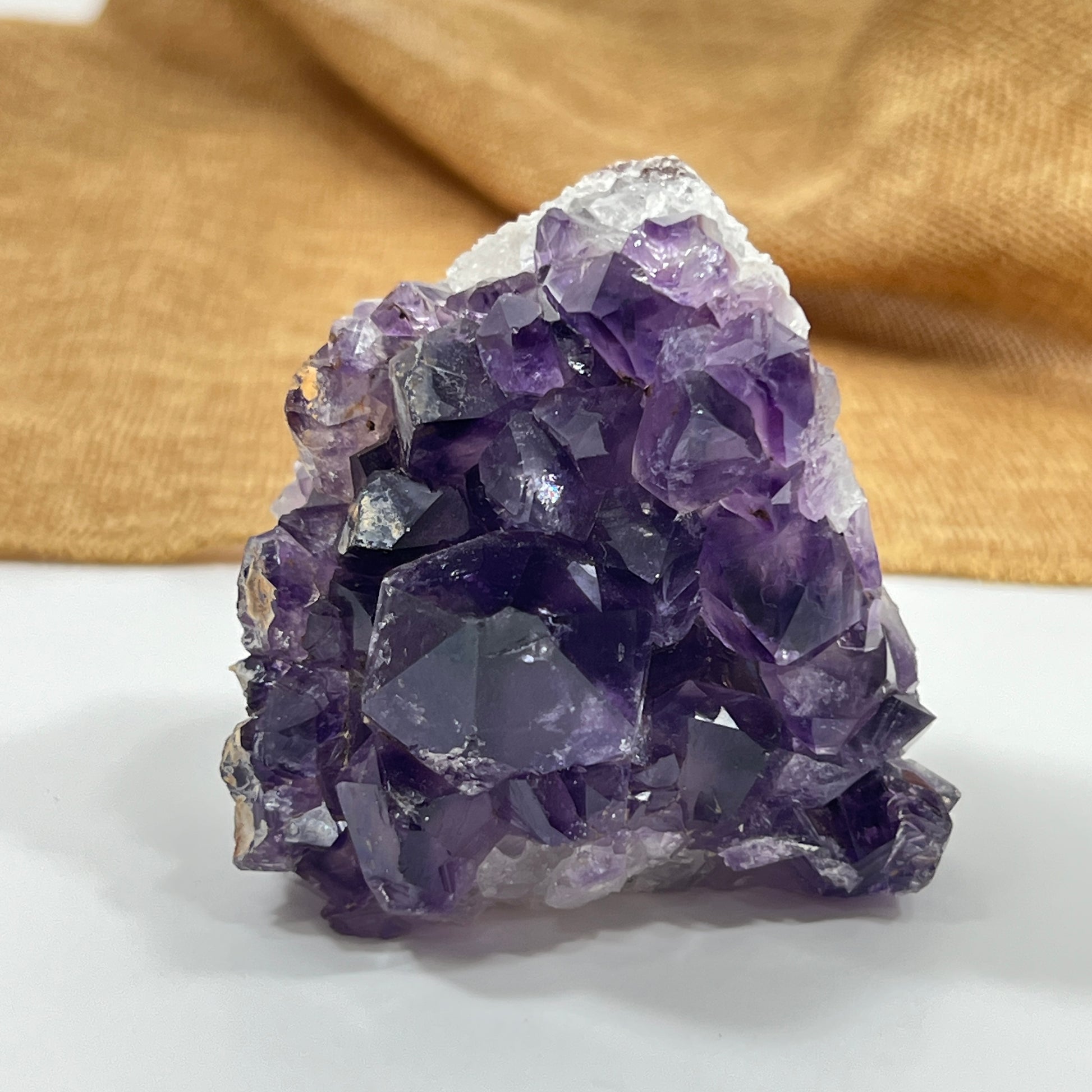 Amethyst crystal cluster on a white surface with a gold fabric background