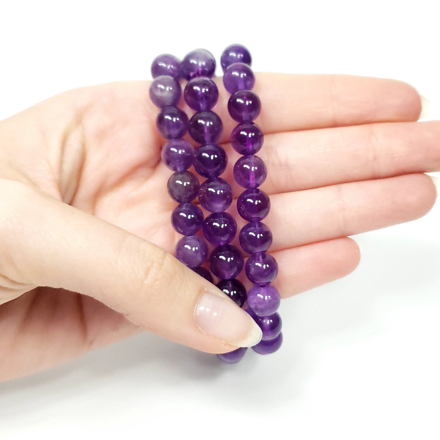 Three purple amethyst beaded stretch bracelets held in a person's hand against a clean white background.