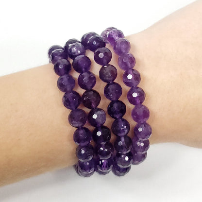 Three stacked Amethyst Gemstone beaded stretch bracelets made of faceted purple gemstone beads, shown worn on a person's wrist against a plain white background.