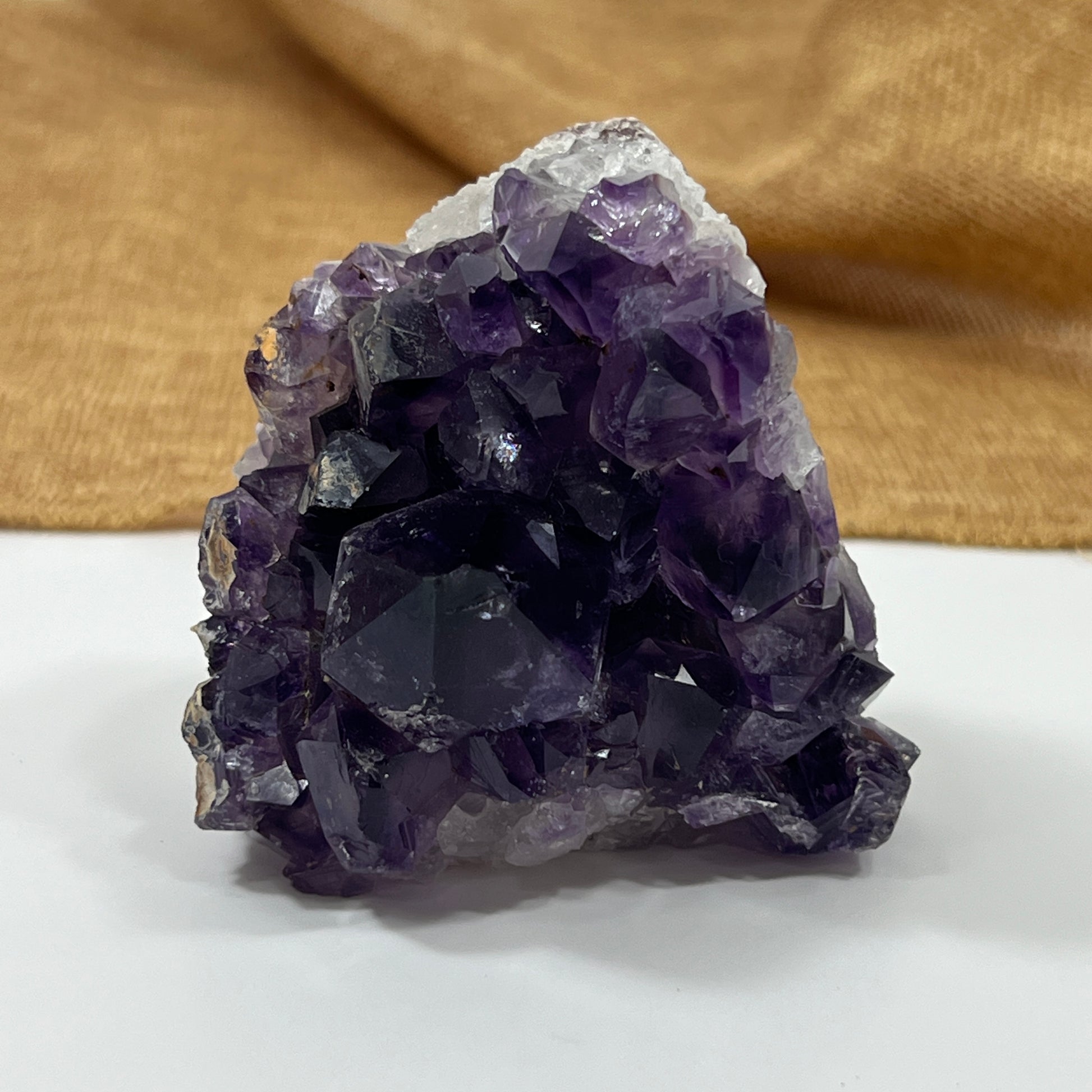 Amethyst crystal cluster on a white surface with a brown fabric background