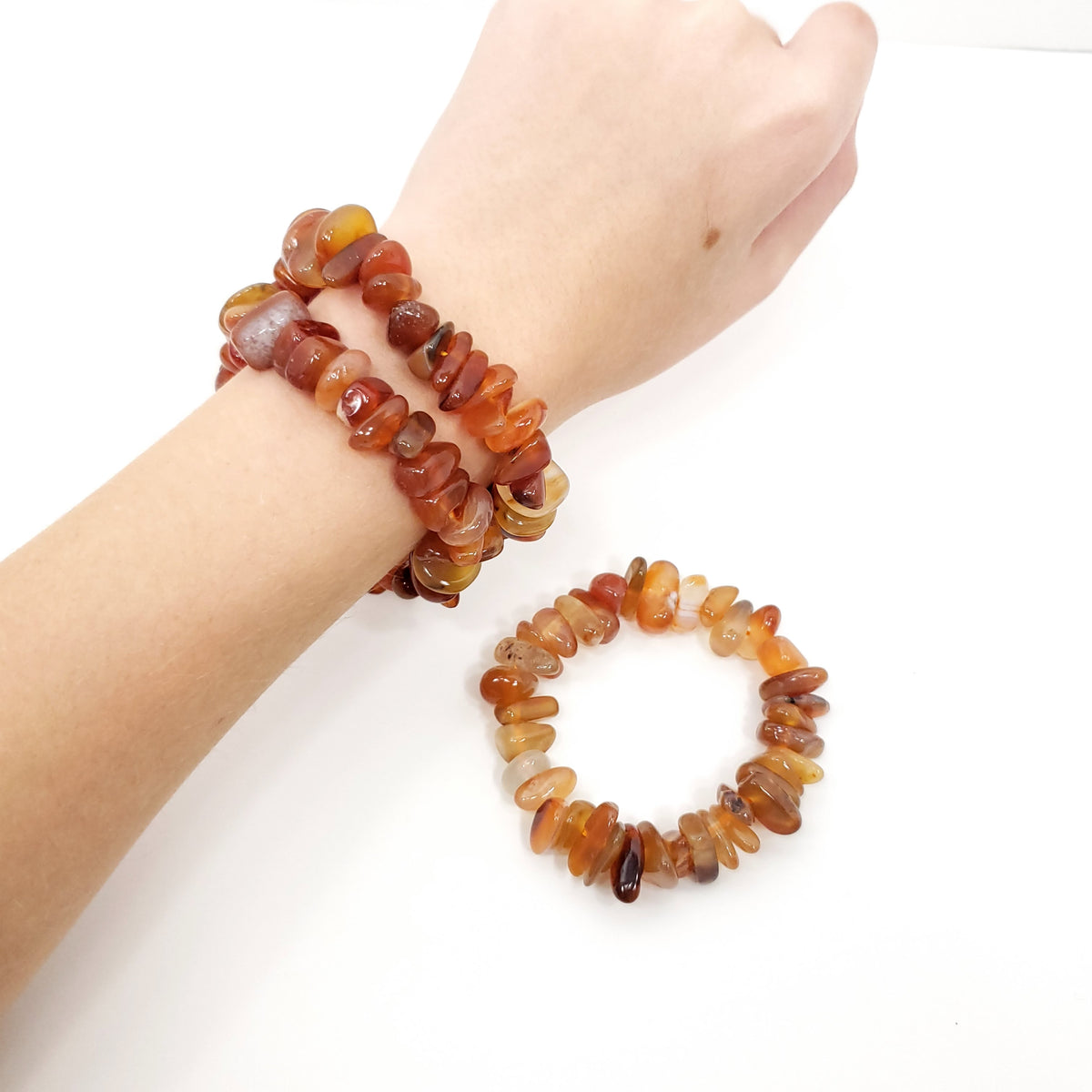 Two beaded stretch bracelets made of polished chunky gemstone chips in warm amber, orange, brown, and translucent tones, shown worn on a wrist and displayed separately on a white background.