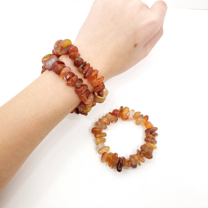Two beaded stretch bracelets made of polished chunky gemstone chips in warm amber, orange, brown, and translucent tones, shown worn on a wrist and displayed separately on a white background.