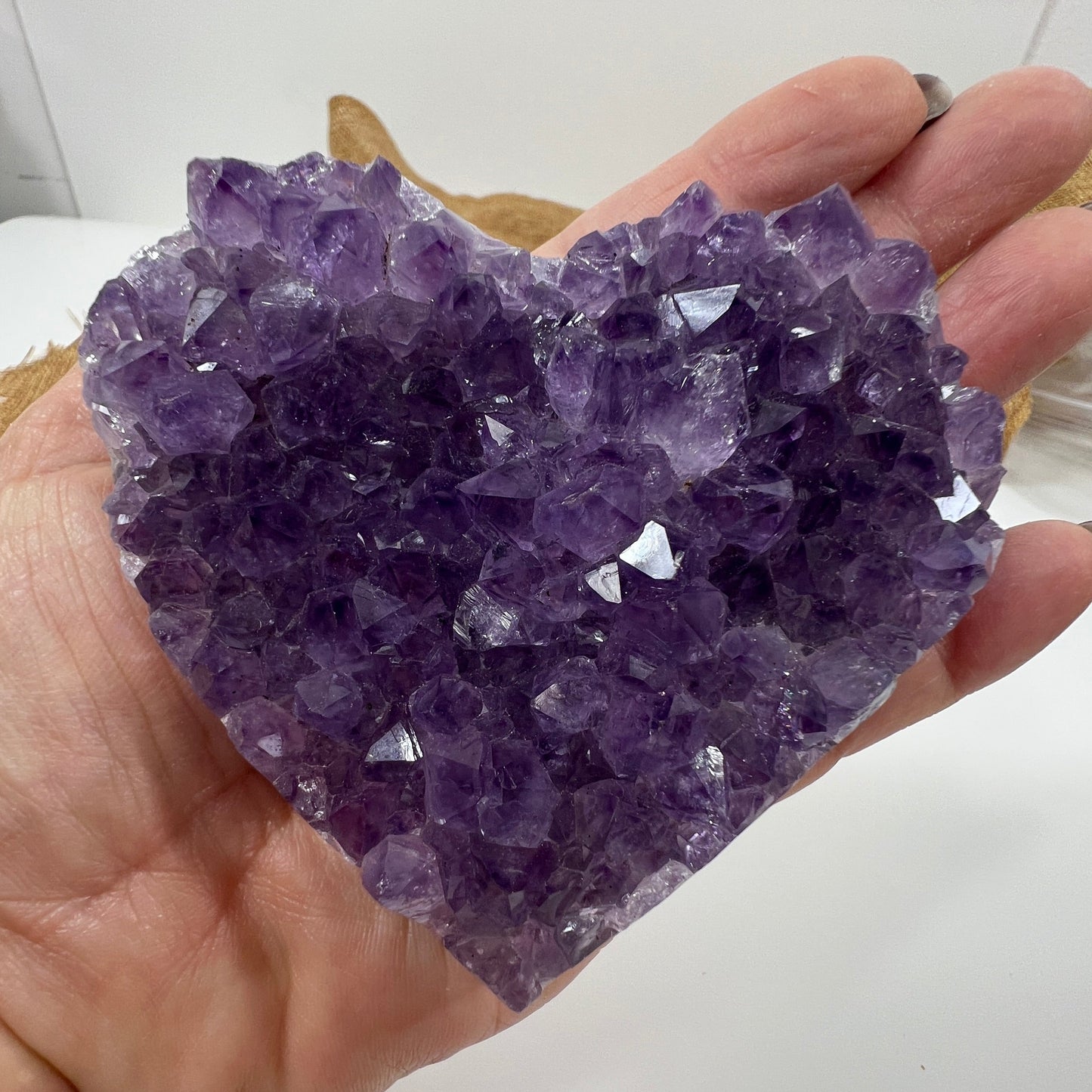 Hand holding a large purple crystal cluster against a white background