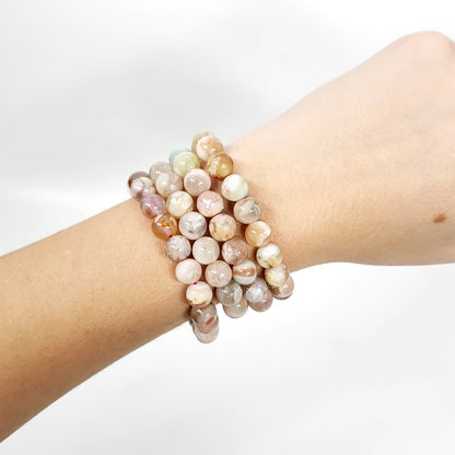 Three beaded flower agate stretch bracelets with marbled pastel gemstone beads, shown worn on a person's wrist against a white background.