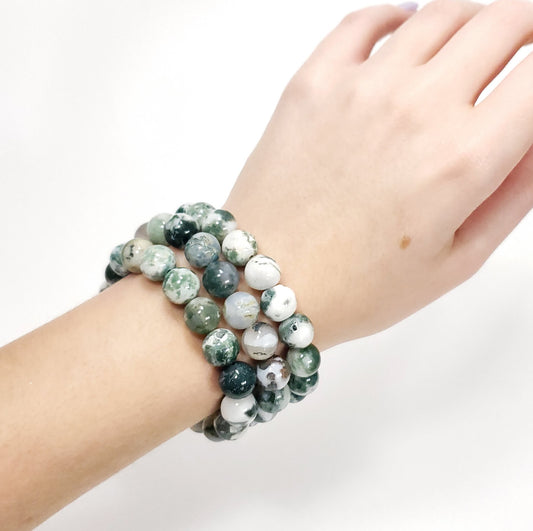 Hand wearing a Green Moss Agtate Crystsal  bracelet with green and white beads on a plain background