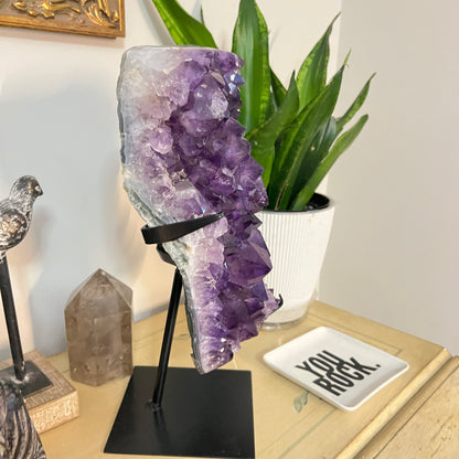 Amethyst crystal on a stand in a home setting with decor items.