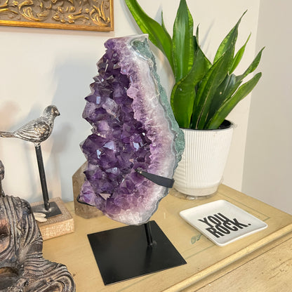 Amethyst crystal on a stand with decorative items on a table