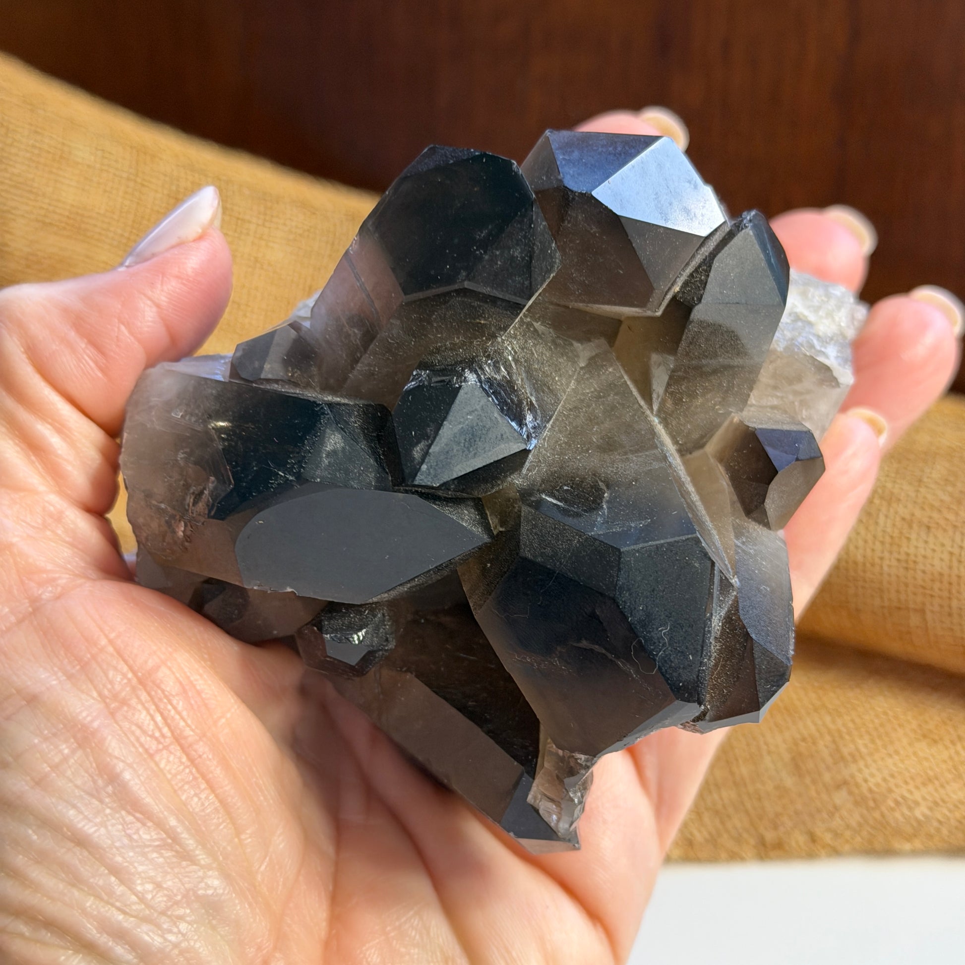 Hand holding a large smoky quartz cluster with points against a blurred background