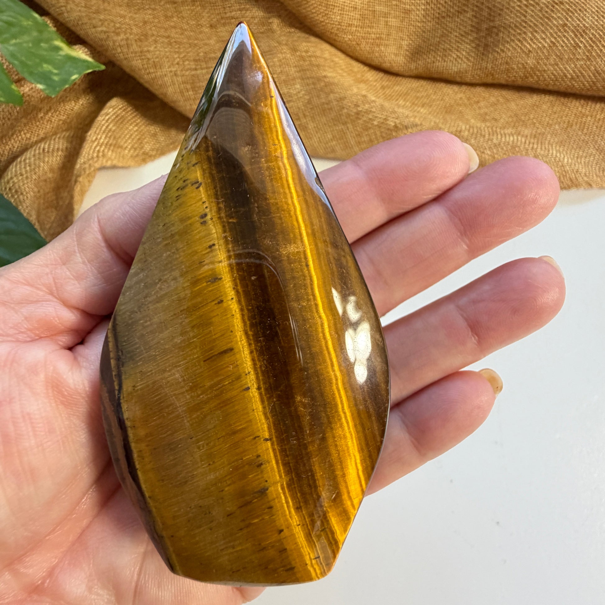 Hand holding small Golden Tiger Eye Flame showing size comparison and natural shimmer of protective grounding stone