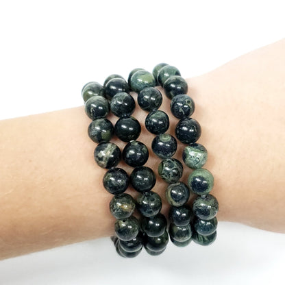 Three beaded 8mm Kambaba Jasper stretch bracelets made of polished dark green and black stone, shown worn on a person's wrist against a plain white background.