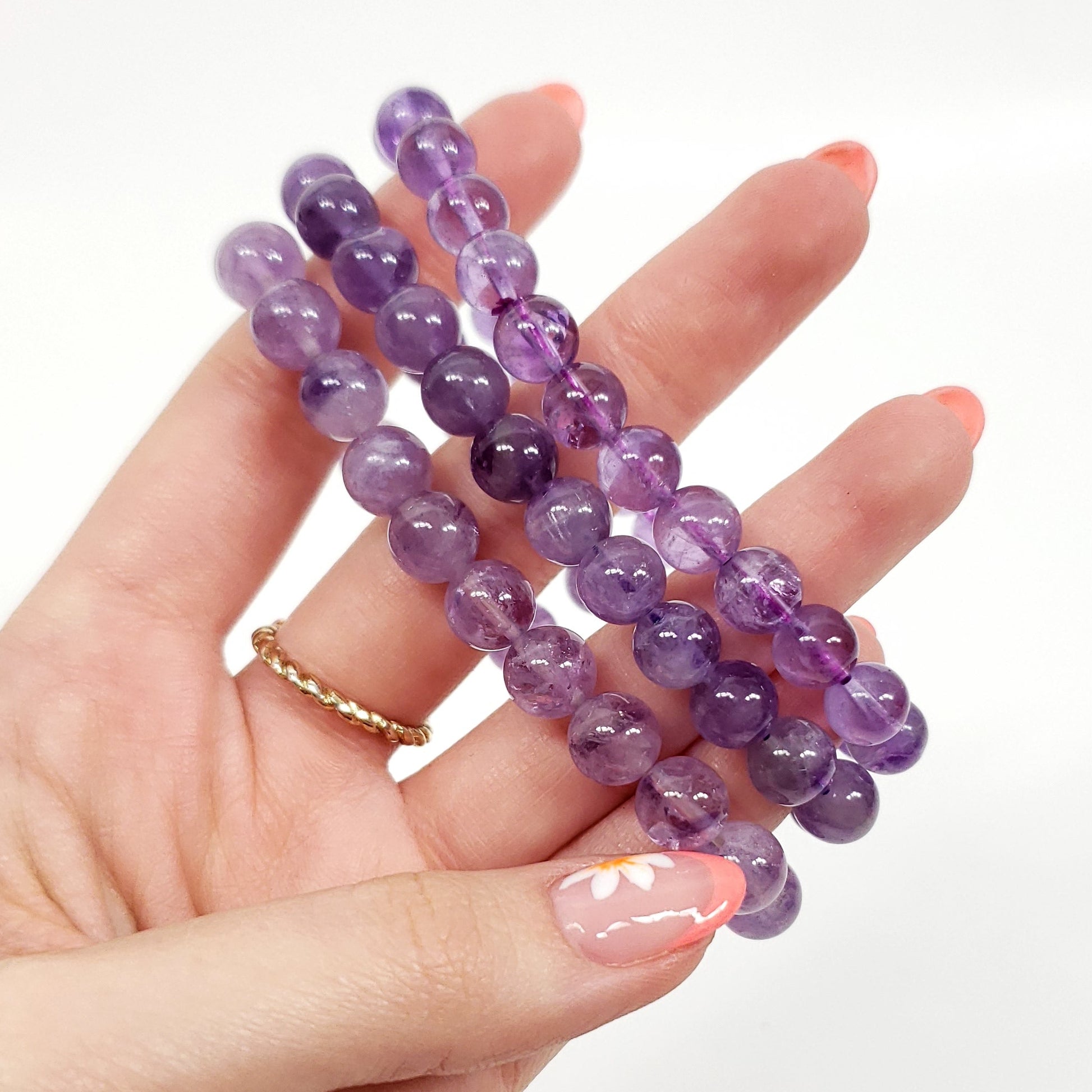 Three light purple amethyst  beaded bracelets held in a hand against a plain white background