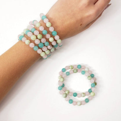 A set of pastel beaded stretch bracelets with pink, mint green, and turquoise-blue round beads of Amazonite, Jade and Rose Quartz,  shown worn on a person's wrist and arranged on a white surface.