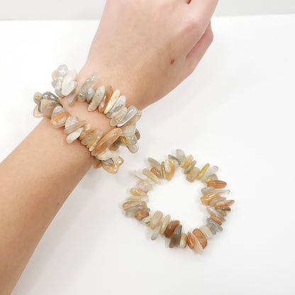 Two bracelets made of polished natural stone chips in neutral earthy tones, shown on a person's wrist with a second band laid flat on a white surface.