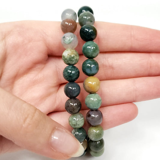Hand holding a pair of green beaded bracelets on a white background