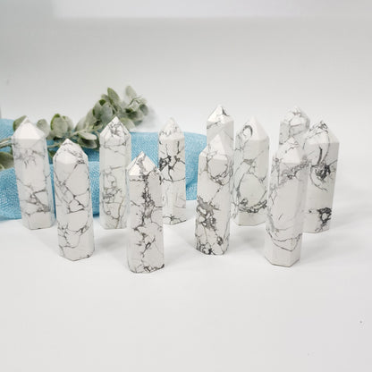 A set of white marble crystal points with gray veining, arranged on a white surface with a light blue textured fabric and green leaves in the background.