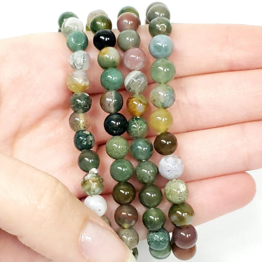 Hand holding a stack of green beaded bracelets on a white background