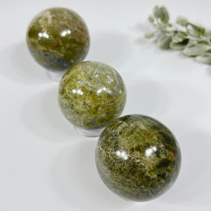 Three green marbled stones on a white surface with a small plant.