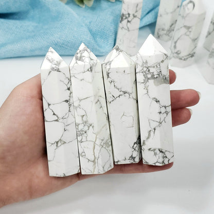 Four white marble crystal points with gray veining, held in a person's hand against a light background with more crystals blurred in the back.